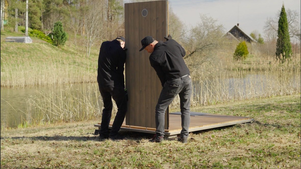 Two installers raising a micro CLT sauna wall panel by hand during assembly